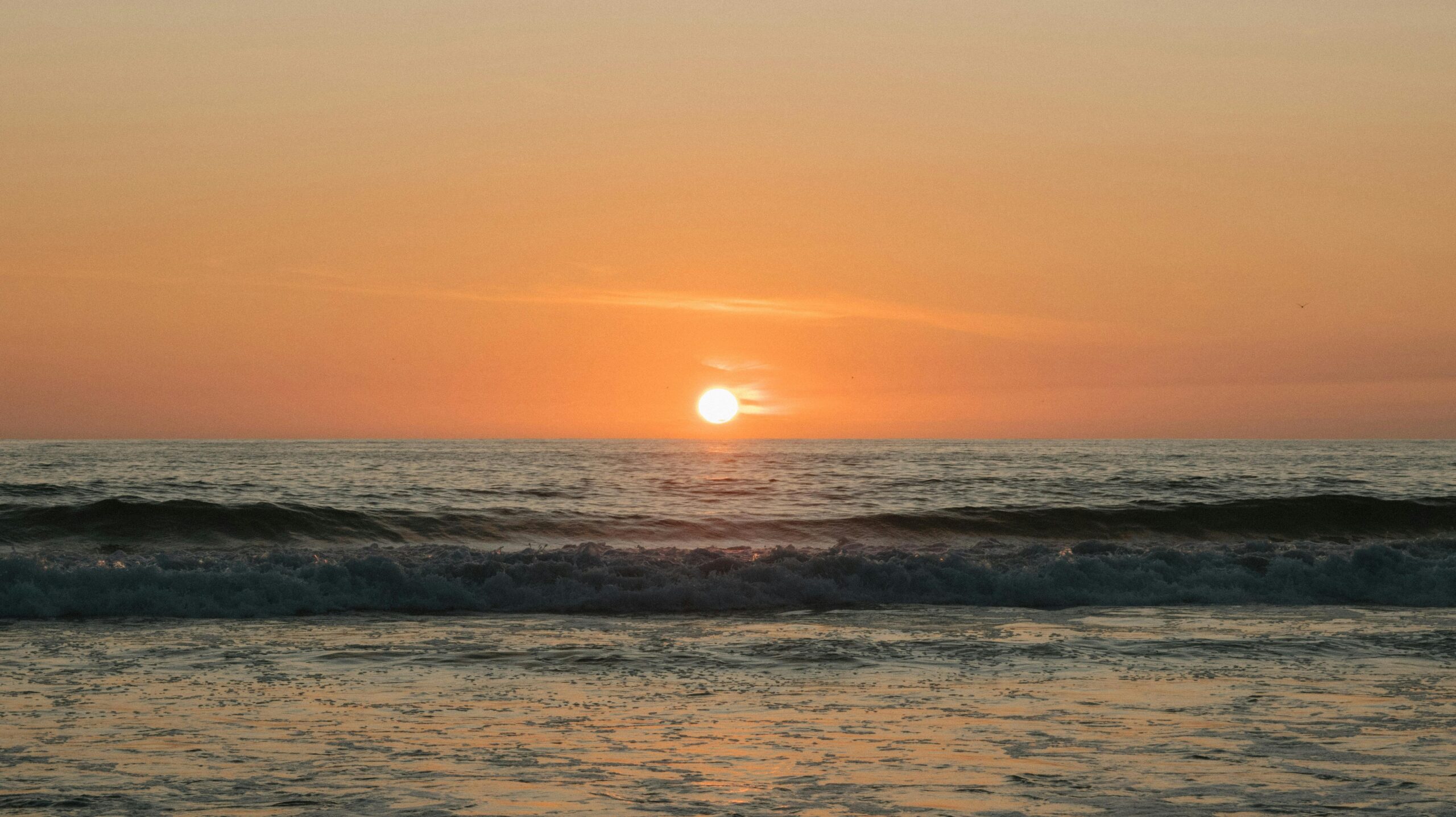 Capture the beauty of a tranquil ocean sunset with soft waves and a glowing horizon.